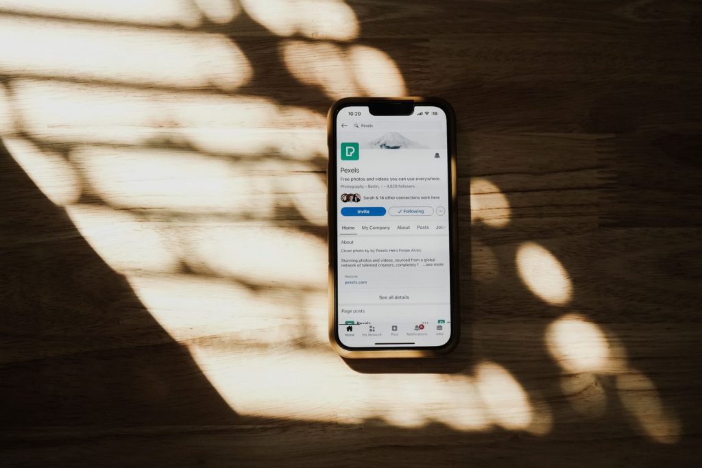 A smartphone displaying a social media profile on a sunlit wooden table.